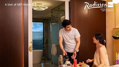 Creative lifestyle photography showing a couple enjoying morning coffee and breakfast in a luxurious hotel suite with ocean views, showcasing the elegant Biophilia Suite experience at Radisson Blu GRT Chennai with modern amenities and spacious accommodatio