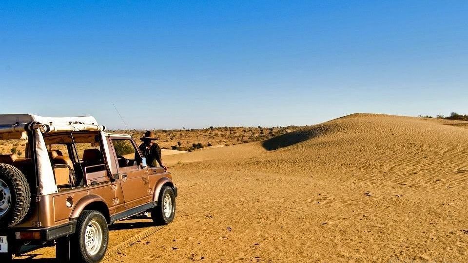 An image of a desert campsite featuring a jeep with a rugged desert landscape and sparse vegetation surrounding it at Manvar Resort & Desert Camp