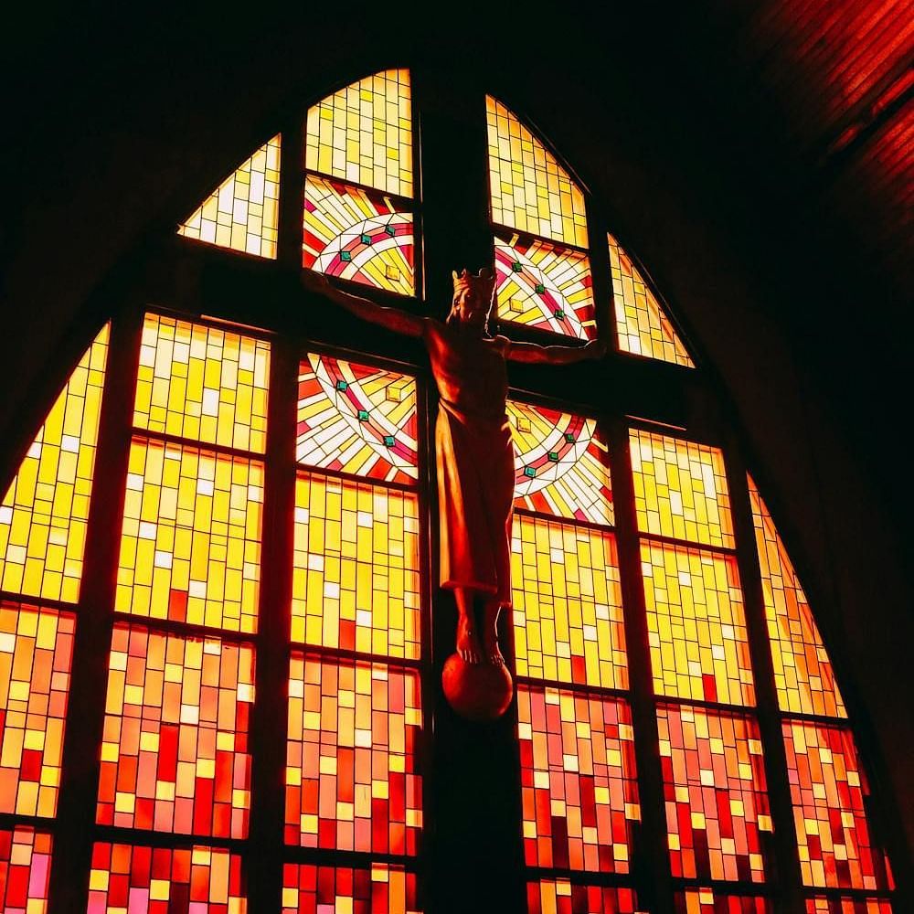 An image of Jesus on the crucifix set against the backdrop of stained glass windows.