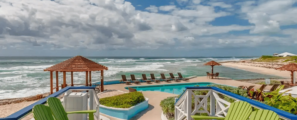 Wooden deck with two bright green chairs facing a turquoise ocean, with a boardwalk and loungers in the distance | Abaco Inn