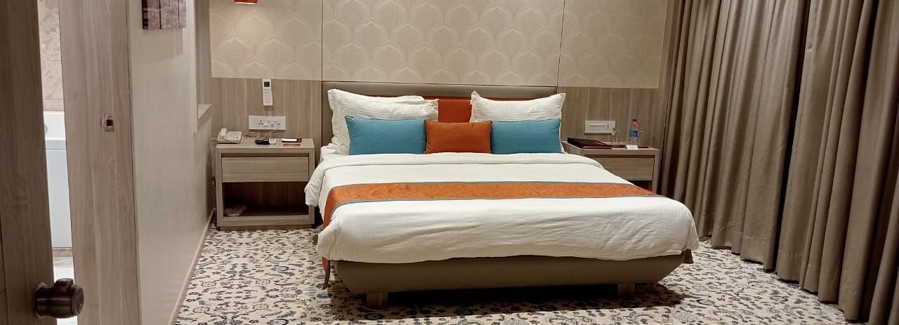 A contemporary hotel bedroom featuring a large bed with white bedding, decorative cushions, and warm ambient lighting.