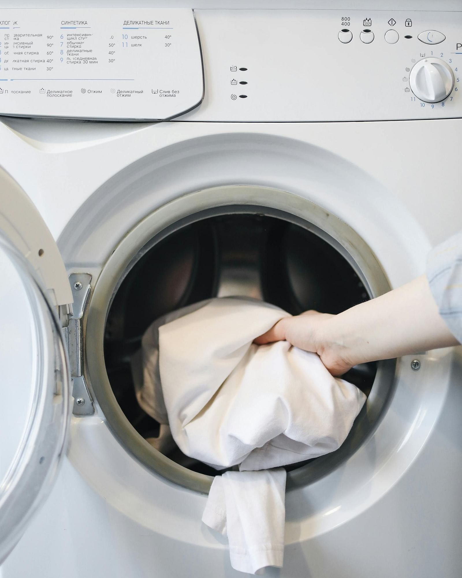 A front-loading washing machine with a hand placing clothes inside.