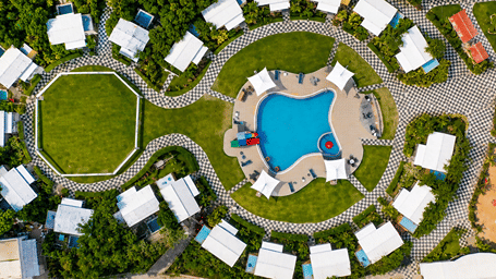 Aerial view of The Mansion House resort layout featuring white circular cottages arranged around a central lawn and swimming pool surrounded by greenery - Lords SKD Resort