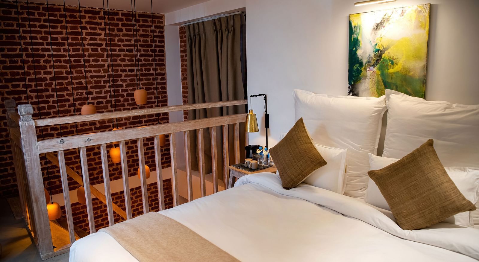 Loft suite where a staircase is leading to it featuring a bed, pillows, and wall hangings - The Nanee