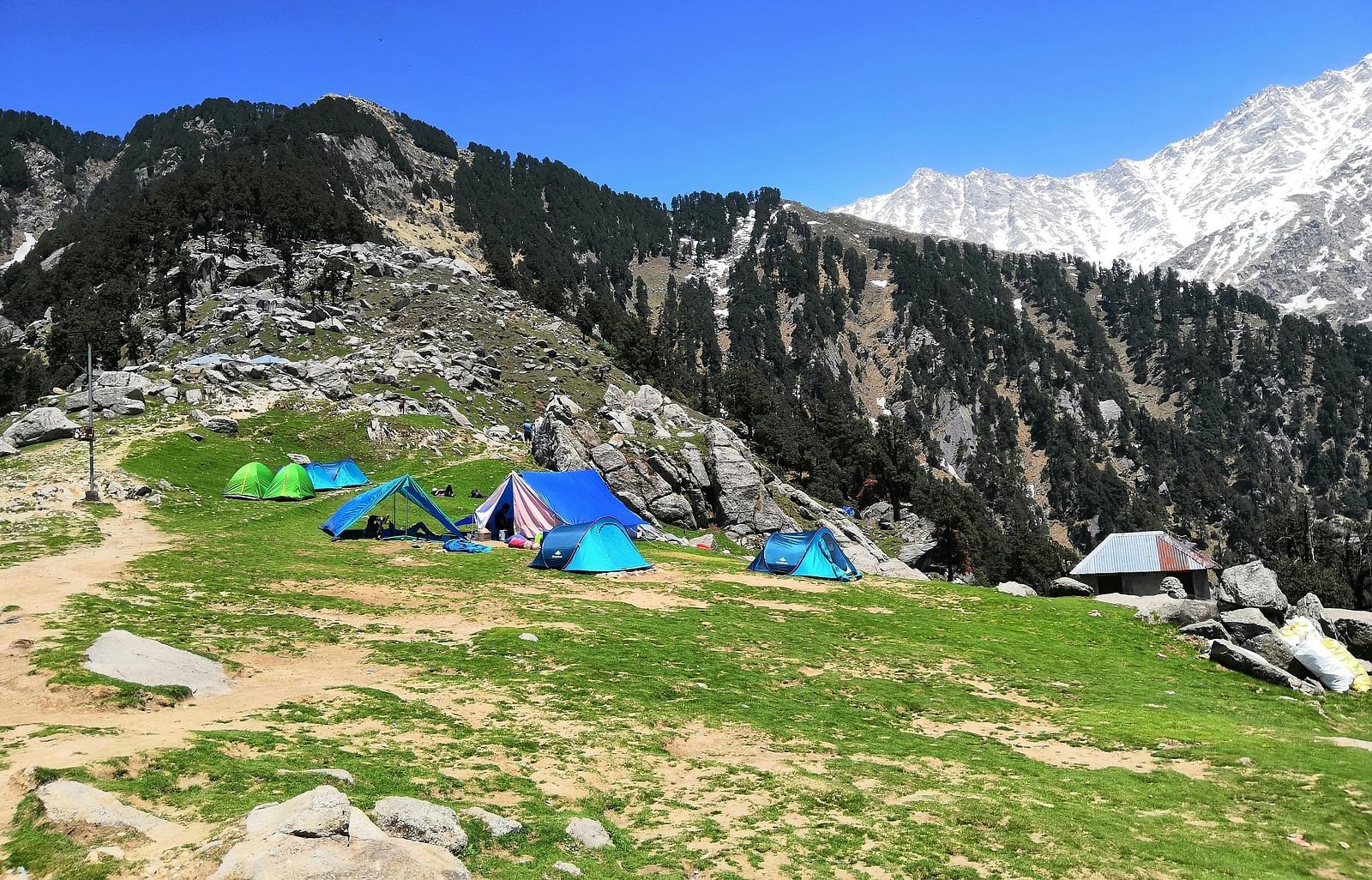 An image of a campsite nestled in a mountainous landscape, with tents pitched and a clear sky.