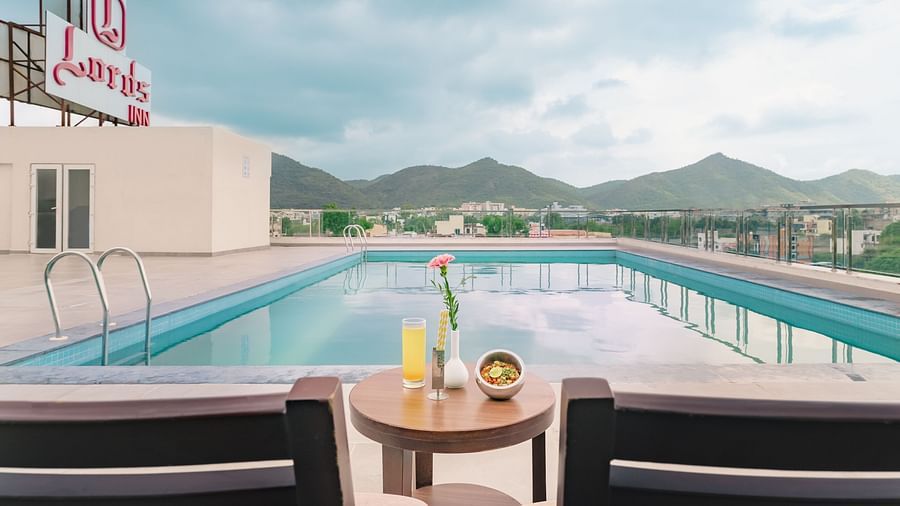 A rooftop pool at Lords Inn Udaipur offers a scenic view of distant hills, with a table set for two in the foreground.