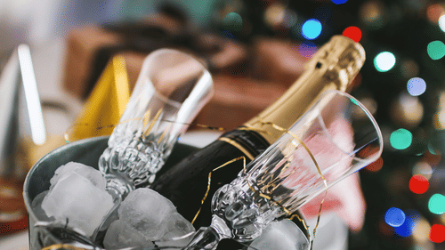 A close up shot of a bucket with a bottle of champagne, ice and champagne glasses
