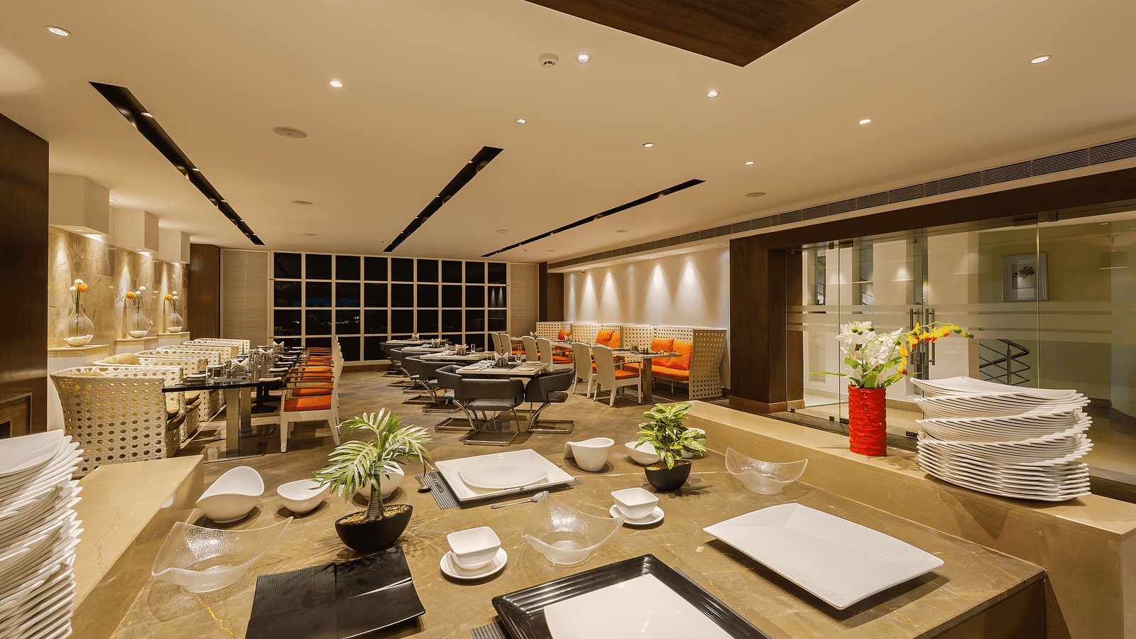 Spacious and modern restaurant interior with buffet serving area, black and white dining furniture and orange accents in seating and decor - TGI Grand Fortuna, Hosur