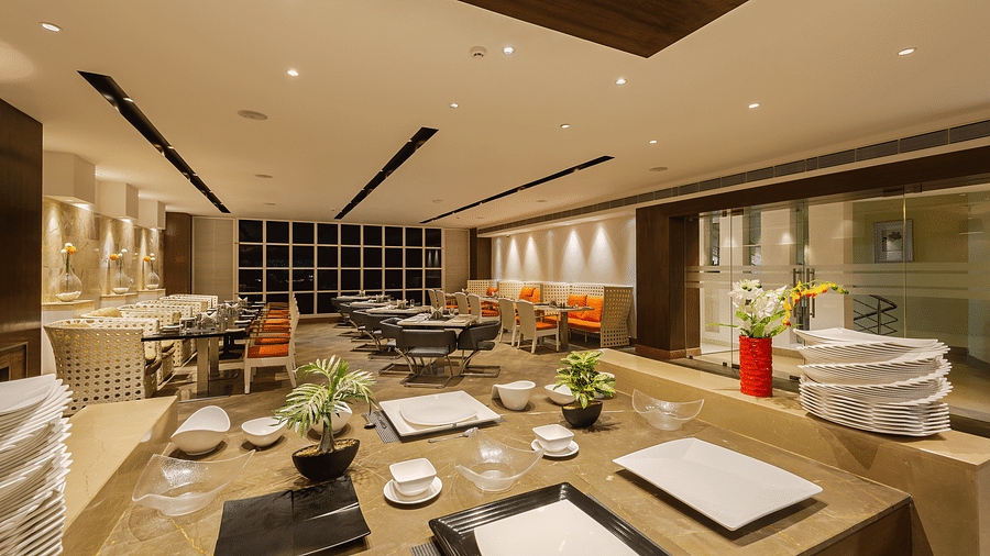 Spacious and modern restaurant interior with buffet serving area, black and white dining furniture and orange accents in seating and decor - TGI Grand Fortuna, Hosur