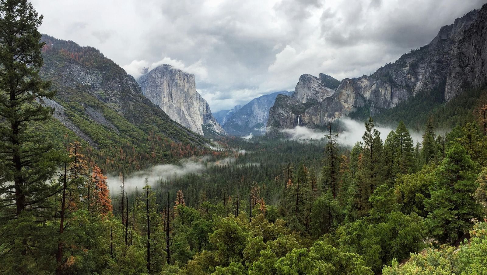 A view of a valley with mountains in the backdrop on a cloudy day