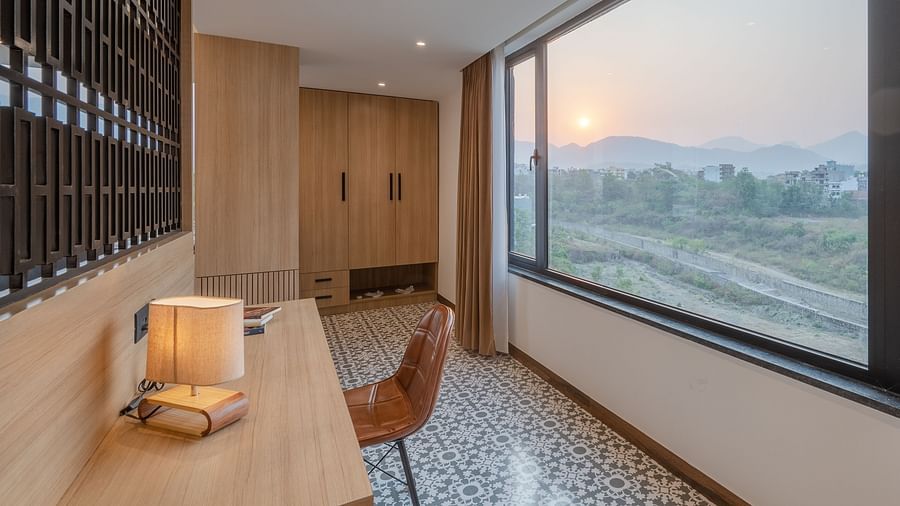 Living area of a suite at Vishranti Hotel, Dehradun featuring a work desk, chair and a large frame window with mountain views.