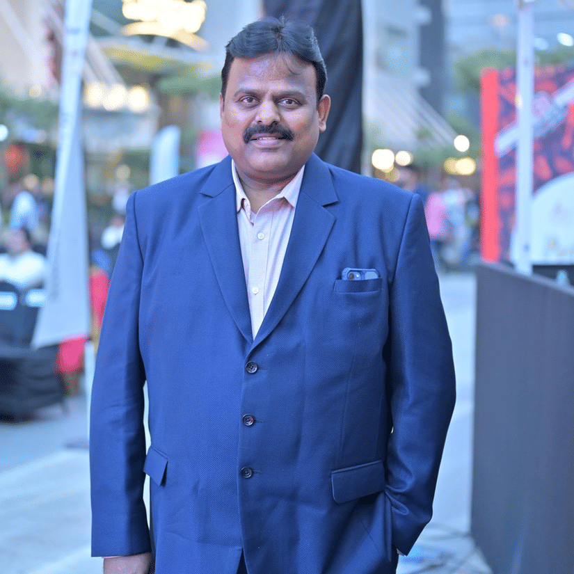 A portrait of R. S. Dharmendra, Chief Operating Officer of Icon Hotels India, standing outdoors in a suit and light-coloured shirt, with an urban commercial setting blurred in the background.