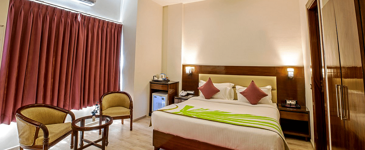The Deluxe room with a double bed along with two cushioned arm chairs kept in front of the window covered by curtains at Regenta Inn DLS.