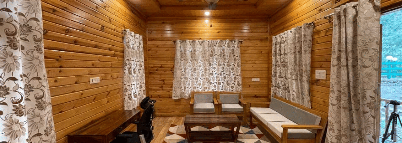 A living room at Dawat e Drung by FrozenFall Resort, Drung, Tangmarg, featuring a sofa, a coffee table, a writing desk with a chair and curtains.