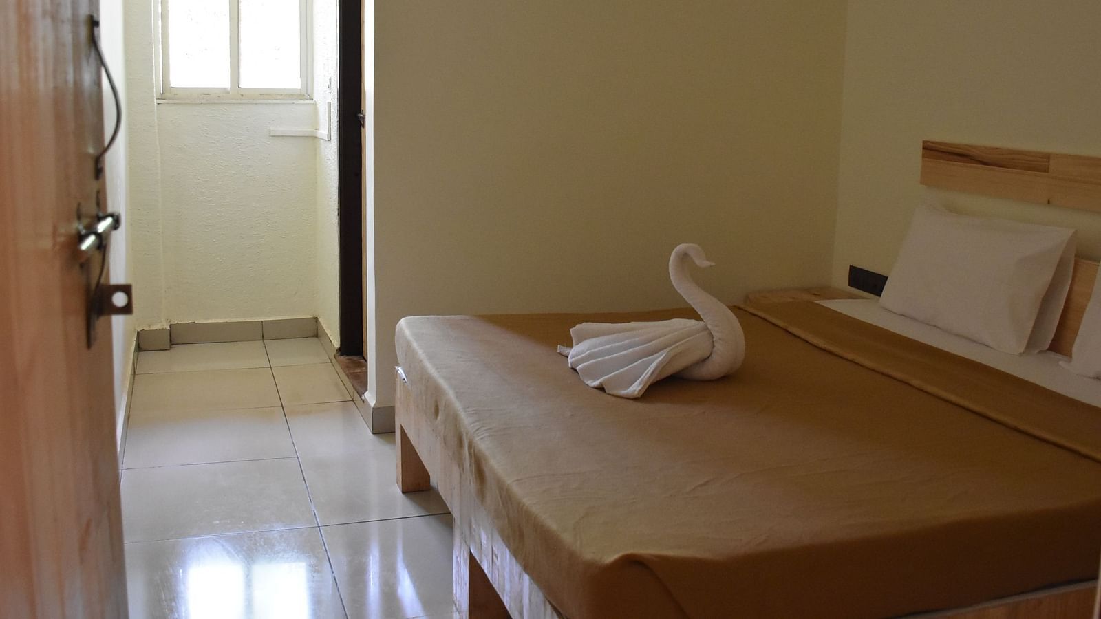 A side view of the room at Riverside Inn with a neatly made bed, a towel folded like a swan, and a pathway leading outside.