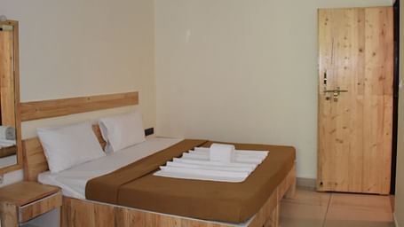 A side view of a neatly made bed at Riverside Inn, featuring arranged pillows, curtains, and neatly placed towels.