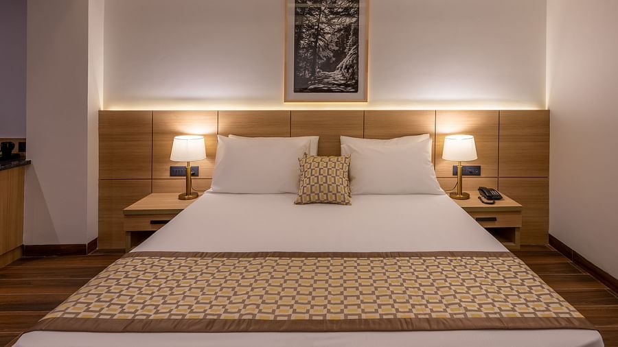 Close up of Premium Room at Vishranti Hotel, Dehradun featuring a king bed with side tables and bed lamps. 