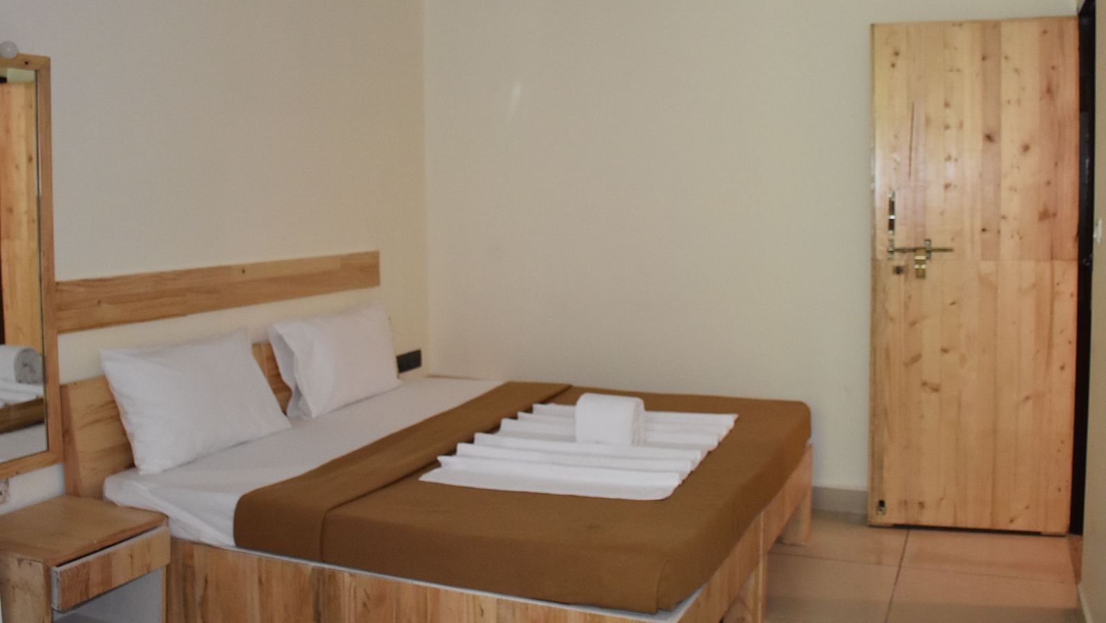 A side view of a neatly made bed at Riverside Inn, featuring arranged pillows, curtains, and neatly placed towels.