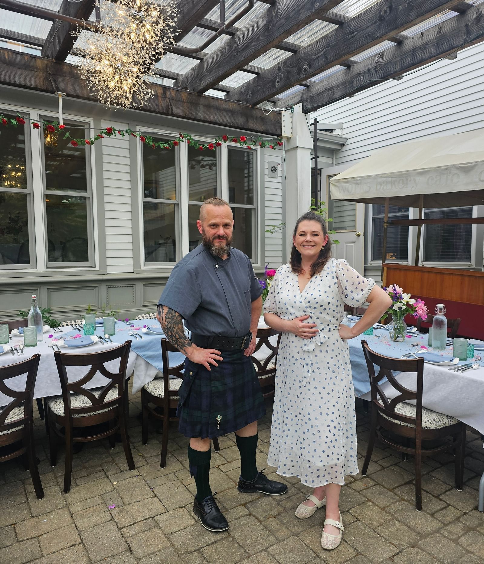 Chef Tom E. White and a woman standing in an outdoor dining area with set tables under a pergola.
