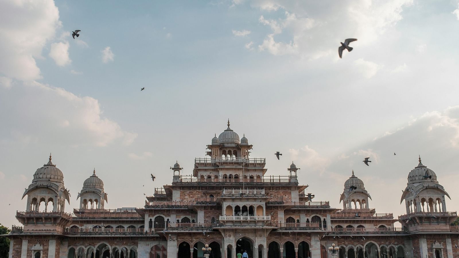 Exterior of a palace during a cloudy day with birds flying over it