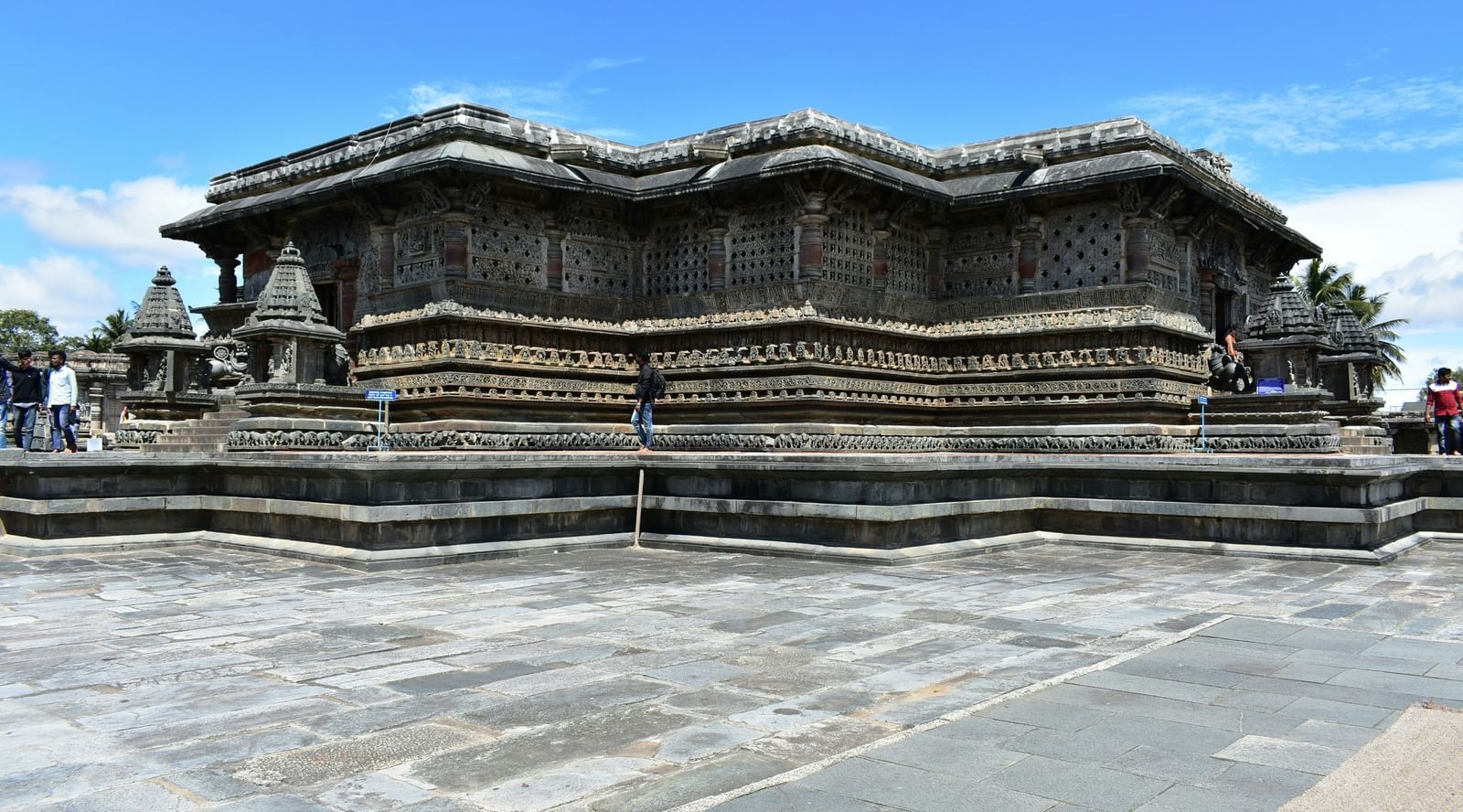Facade of Chennakesava Temple in Belur with a stone courtyard in front of the temple and under a blue sky on a sunny day