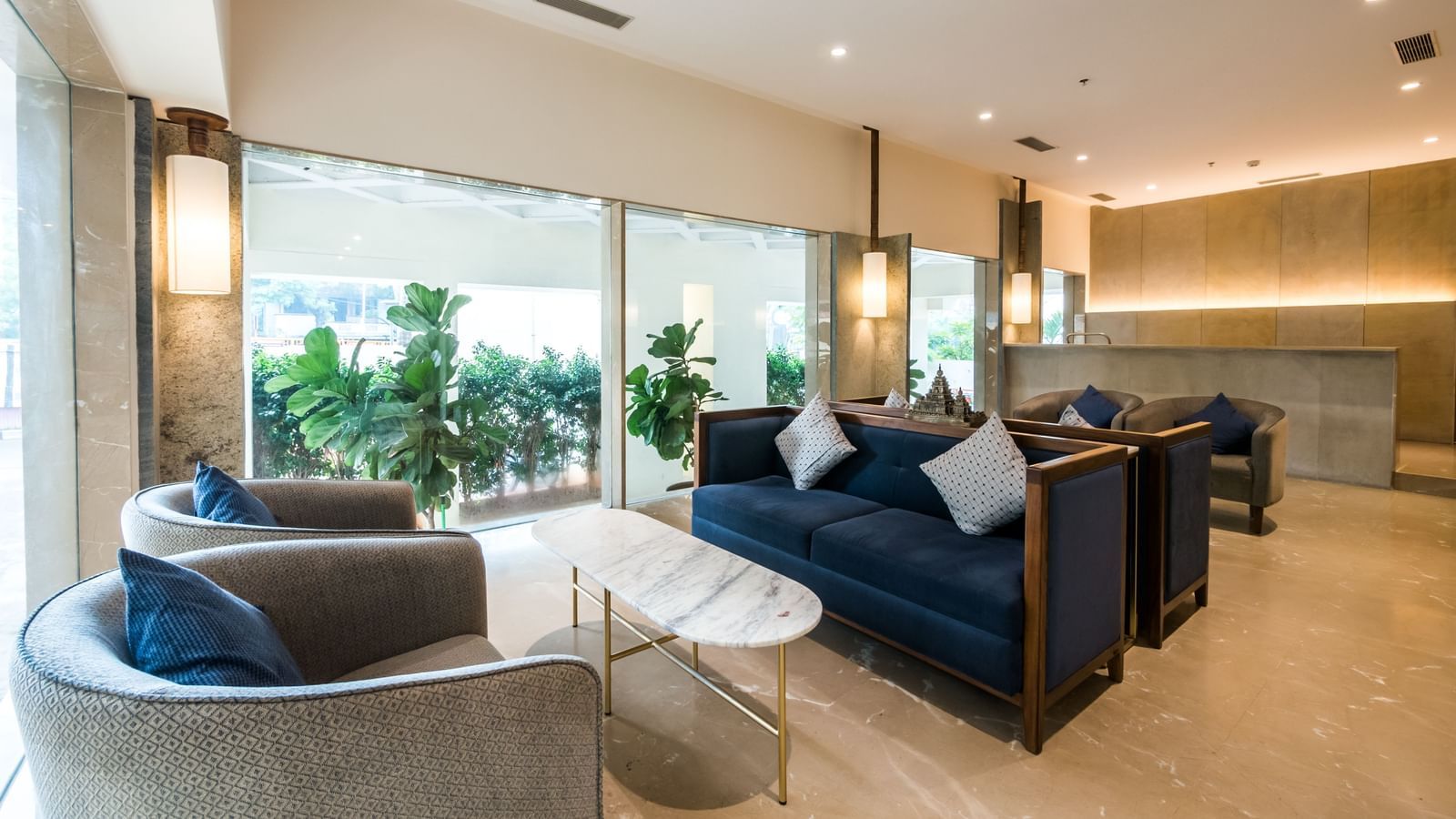 A bright and airy lounge area with plush blue sofas and large windows offering an outdoor view at Shilton Dee Cee.