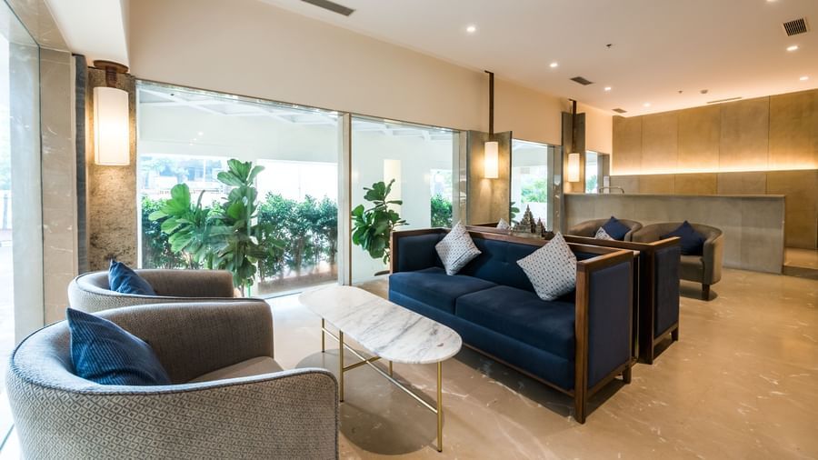 A bright and airy lounge area with plush blue sofas and large windows offering an outdoor view at Shilton Dee Cee.