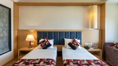 Twin beds with bedside lamps and a wall panel at Golden Tulip, Udaipur.
