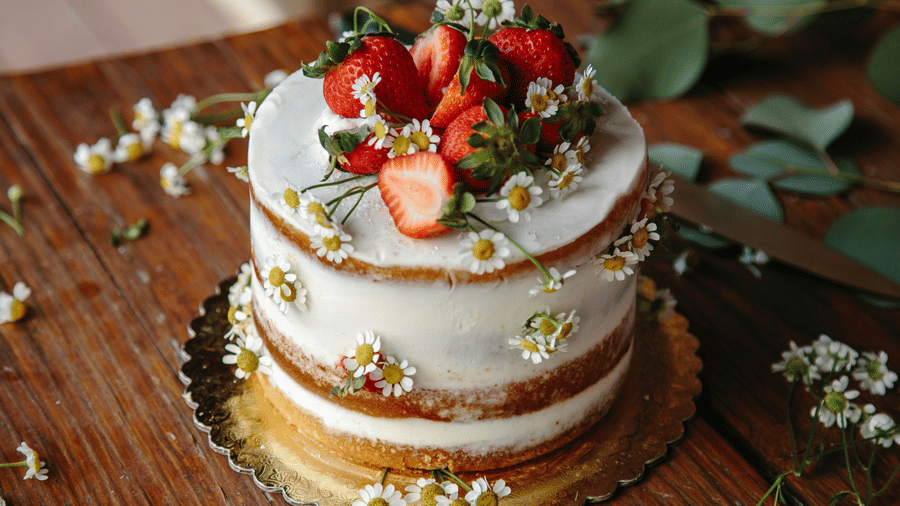 A cake garnished with strawbeery placed on a wooden table. 