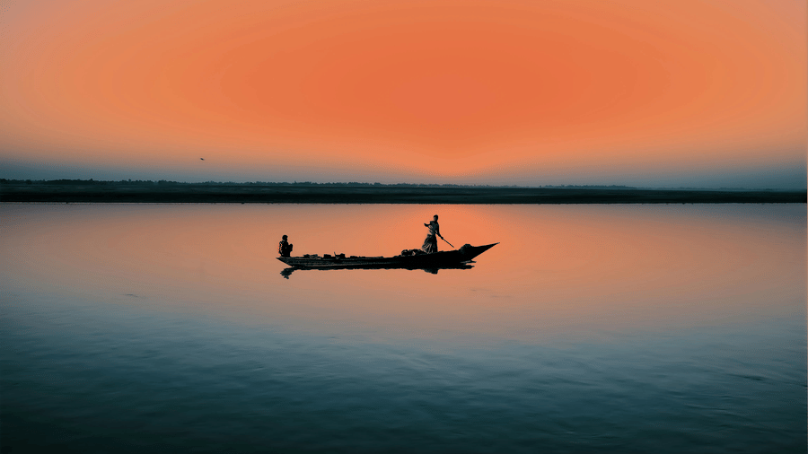 A silhouette of a fisherman in a small boat on a calm lake, set against a vibrant, deep orange sky.