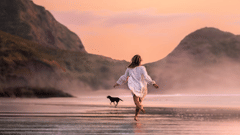 A woman running behind her dog on the beach
