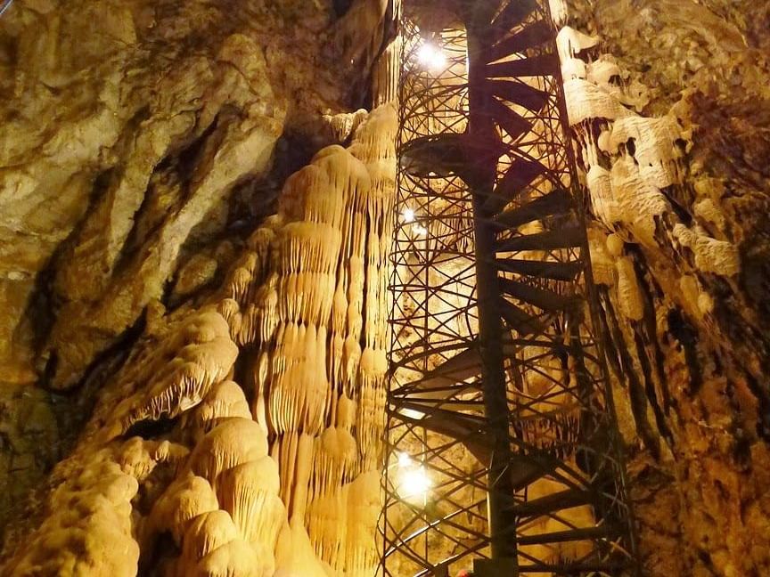 A circular staircase inside a cave with a light shining down the cave.