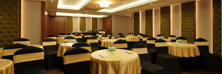 Spacious conference hall with U-shaped wooden table, cushioned black chairs, projector, white screen, and recessed ceiling lights – Magnus Nexstar Suites, Kalyani Nagar