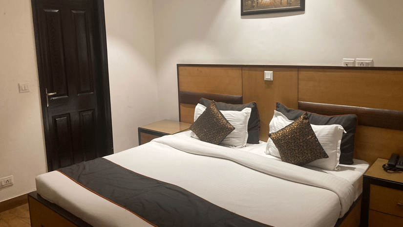 A bedroom at The The Hermitage by The Cosy Hotels (Near Lotus Temple) featuring a neatly-made bed with matching cushions and a bed runner, wooden headboard and a painting on the wall.