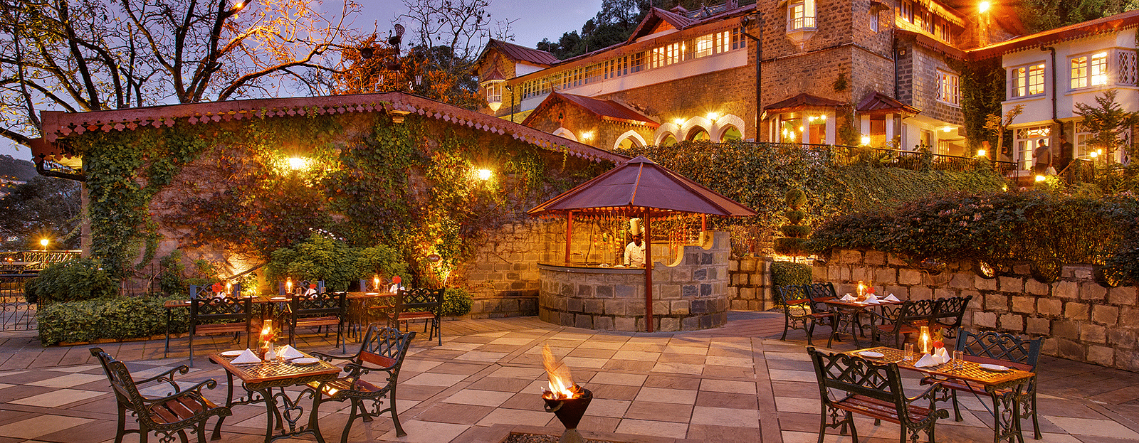Hotel facade illuminated with warm lighting, and a few tables arranged in the evening.