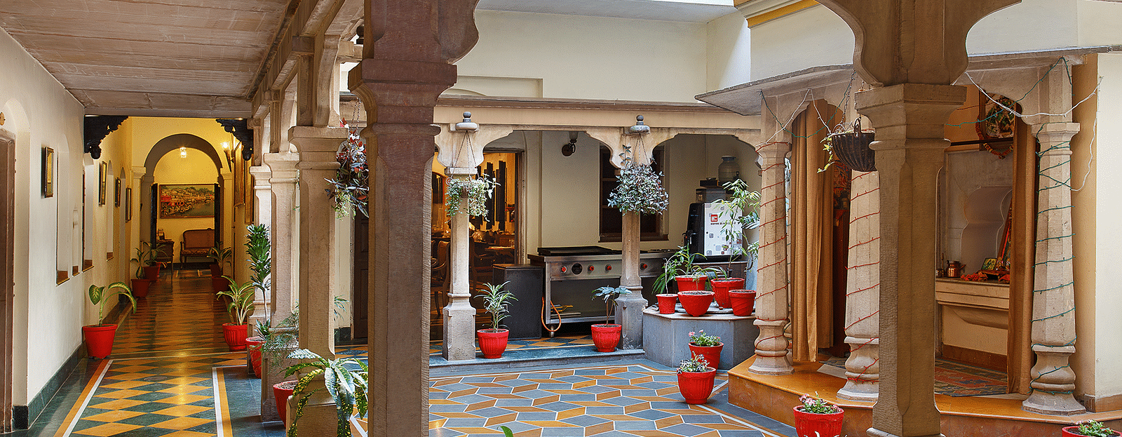 A passage with an open roof space at The Haveli Hari Ganga in Haridwar features block tiles and lush plants, creating a tranquil atmosphere that invites guests to enjoy the beauty of nature while providing shelter and light.