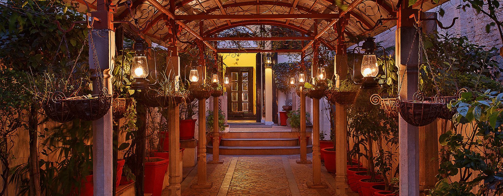 An evening view of a pathway at The Haveli Hari Ganga in Haridwar is beautifully surrounded by lush plants, creating a serene and inviting atmosphere as the soft glow of twilight enhances the natural beauty of the surroundings.