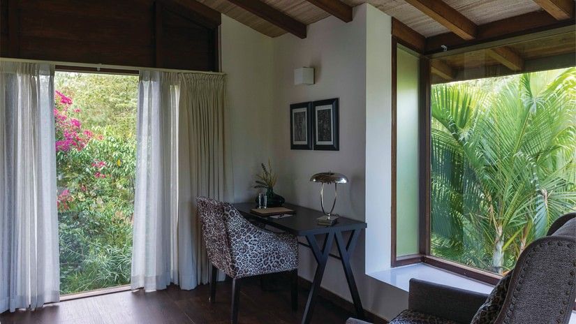 interior of one of the rooms at The Serai Bandipur featuring seating space next to large windows with a green view