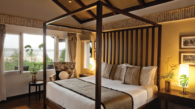 An overview of a bedroom with a four poster bed, side lamps and tables at one of the rooms at The Serai Kabini, ideal for Weekend Trips from Bangalore for Couples.