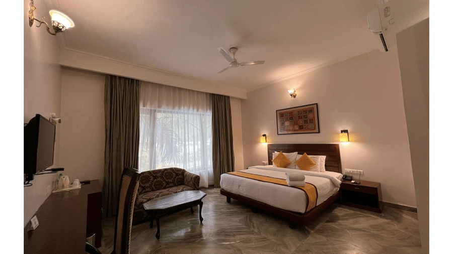 A well-furnished guest room with a double bed, seating area, and natural light at AS Hotels, Khajuraho.