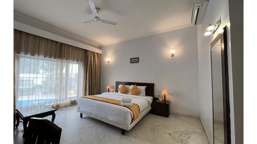 A bright, room with a double bed, warm lighting, and a large window offering a clear poolside view at AS Hotels, Khajuraho.