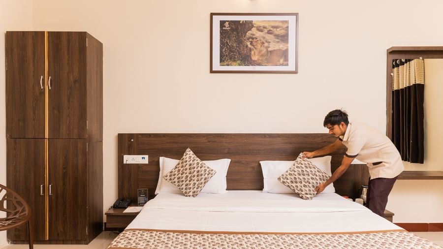 A view of a staff arranging the pillows in a bed with a wall art above it and a wardrobe on the side at Daksh Resort & Amusement Park, Sasan Gir.