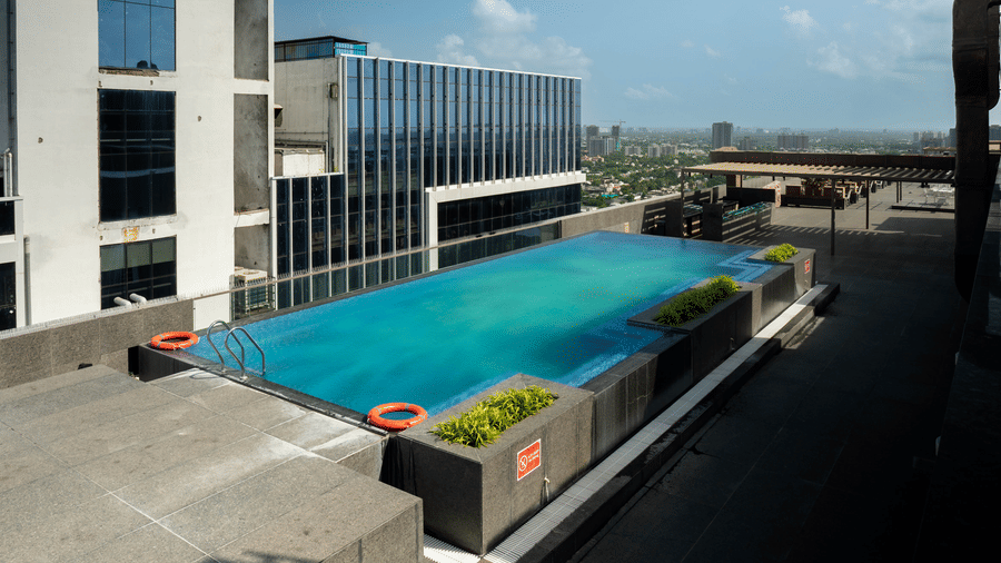 A bright outdoor rooftop swimming pool surrounded by modern glass architecture during the day - Praveg's Grand Eulogia, Ahmedabad