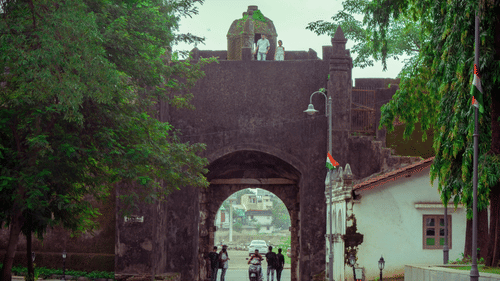 Historic stone gateway of Moti Daman Fort surrounded by trees and visitors.