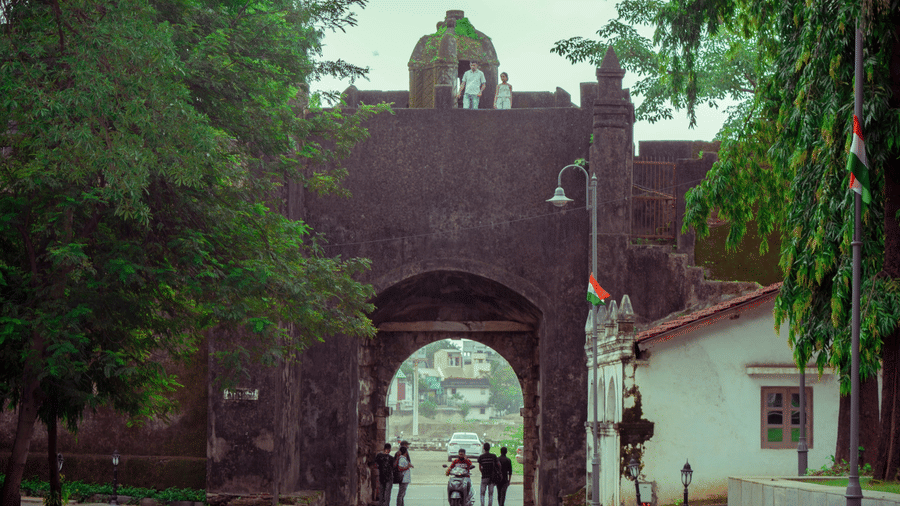 Historic stone gateway of Moti Daman Fort surrounded by trees and visitors.