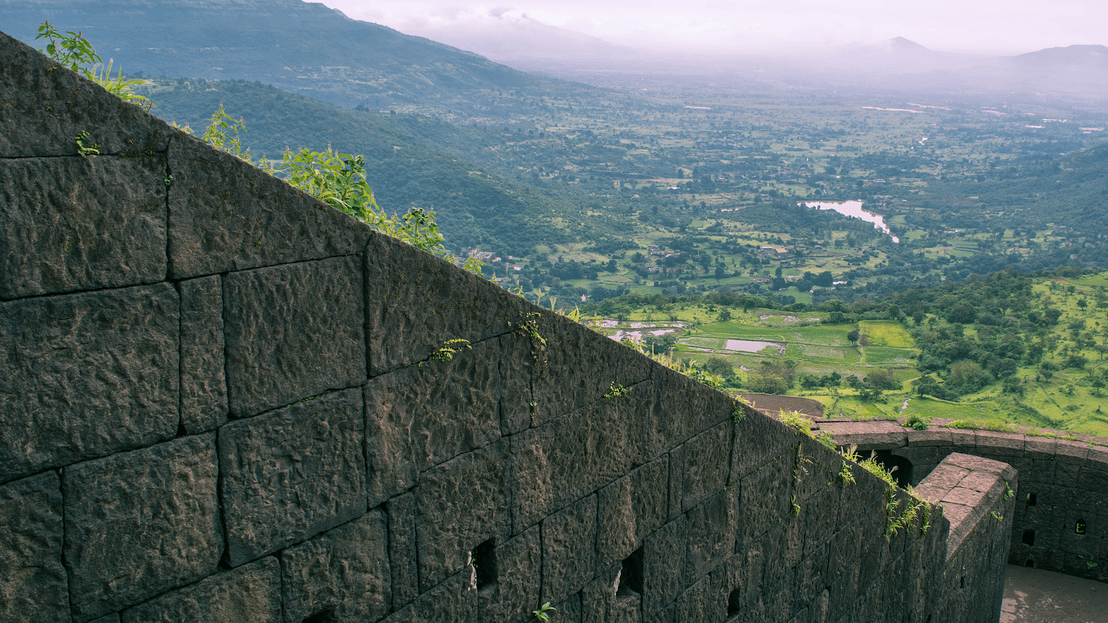 A donward sloping stone wall with a view of the valley and clear skies in the background