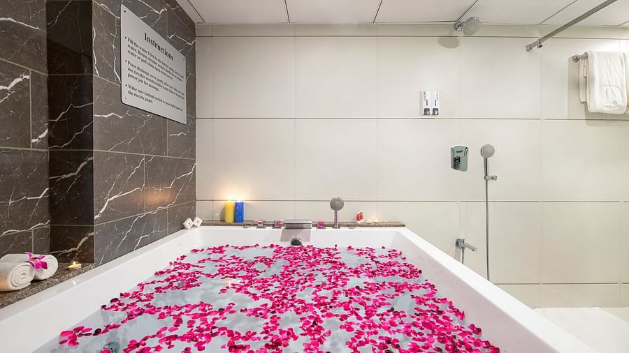 A luxurious bathtub filled with pink flower petals in a bright bathroom - SK Lords Inn Ahmedabad