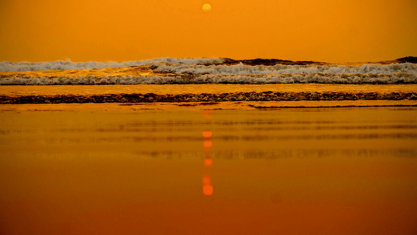 A shot from the surface of the shoreline at a beach in Goa showcasing the twilight view of the sun setting in the horizon and the waves crashing on the shoreline.