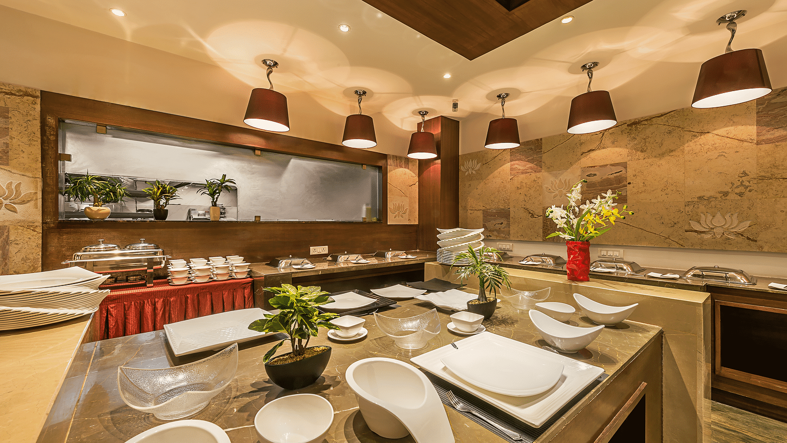 Elegant buffet area in a restaurant with wooden accents, red lampshades and a variety of white serving dishes arranged for use - TGI Grand Fortuna, Hosur
