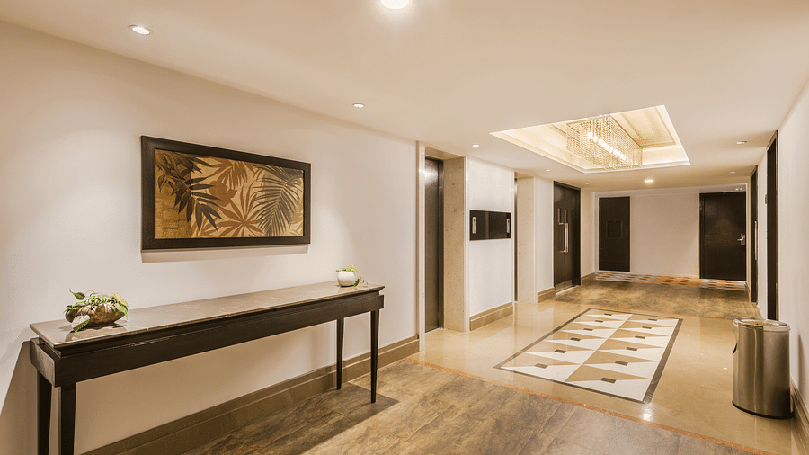 A hotel corridor with decorative artwork, a long bench and a patterned floor leading to elevator doors - TGI Grand Fortuna, Hosur